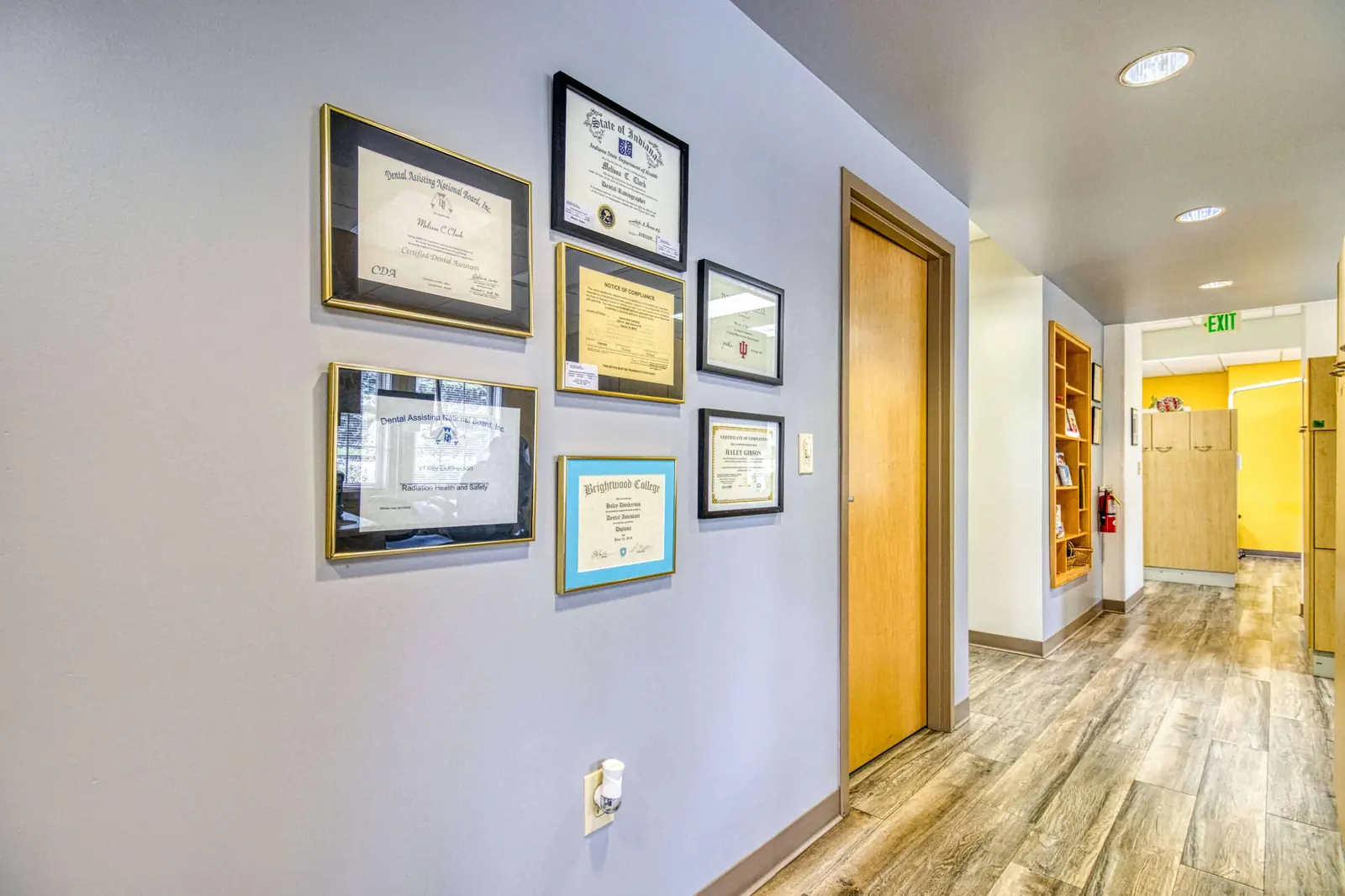 A corridor wall of framed qualifications outside the treatment rooms