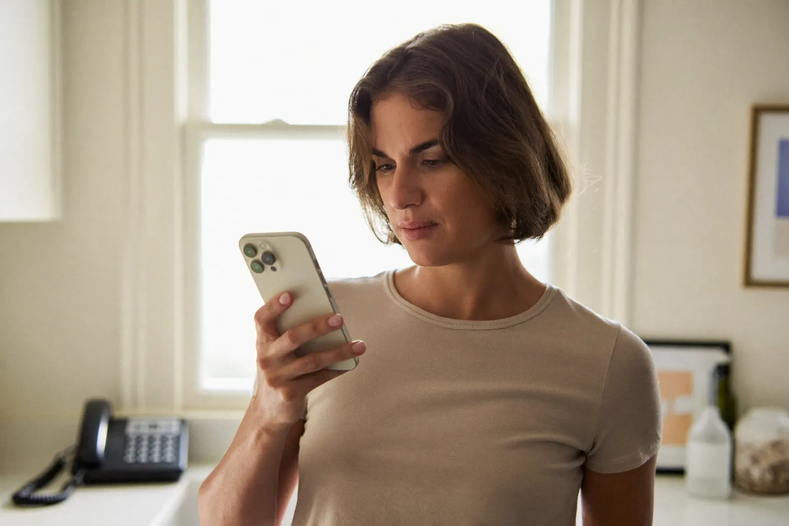 A woman searching for a dentist on her phone in a bright kitchen