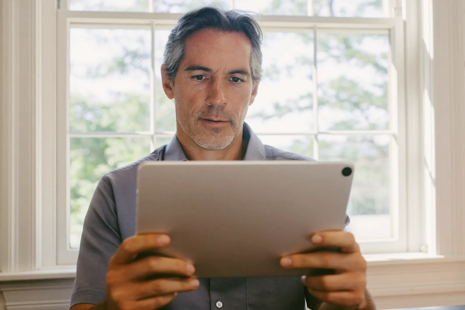 A man reading a practice’s reviews on a tablet by a bright window